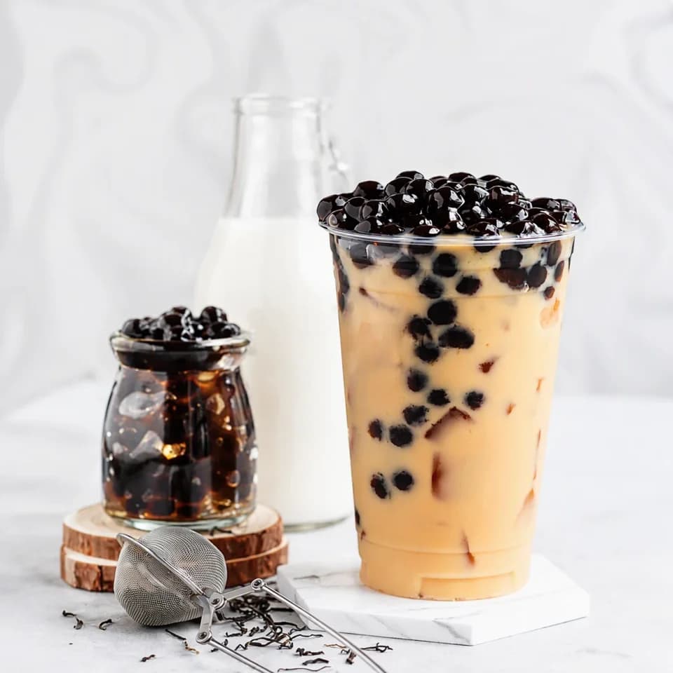 Enhanced pearl milk tea in a light setting beside a milk bottle, a jar of pearls and a tea strainer